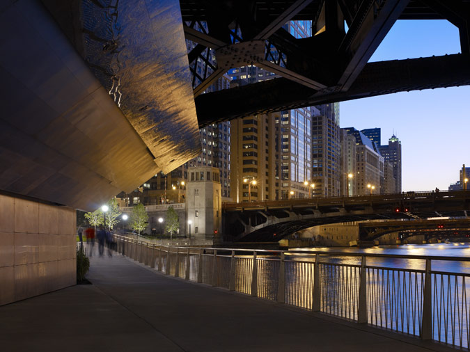 The Riverwalk canopies illuminate a shadowy area under a bridge with washes of artificial light at night.