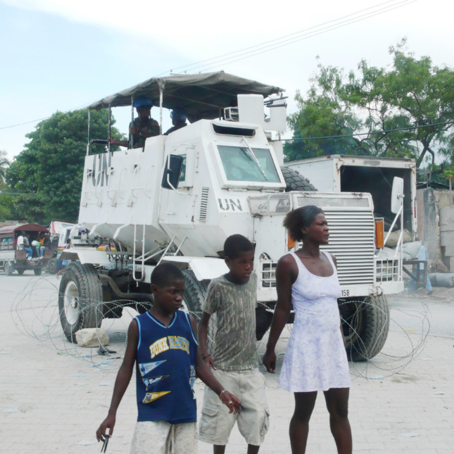 In Port-au-Prince, Haiti, people stand in front of an armored personnel carrier (APC) deployed in the UN-MINUSTAH peacekeeping mission. This APC has been surrounded by barbed wire and placed on wheel chocks, converting it, at least temporarily, from a vehicle to a quasi-architectural technology—a mobile tower.