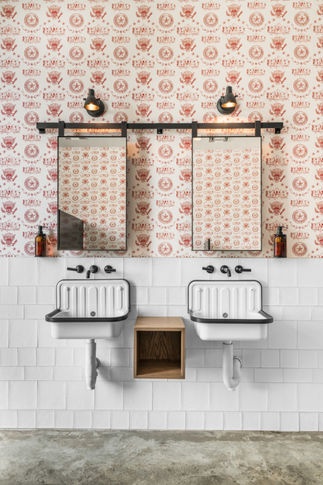 Farmhouse sinks and custom wallpaper in a graphic, Texas-themed pattern complement glazed tile in each restroom.