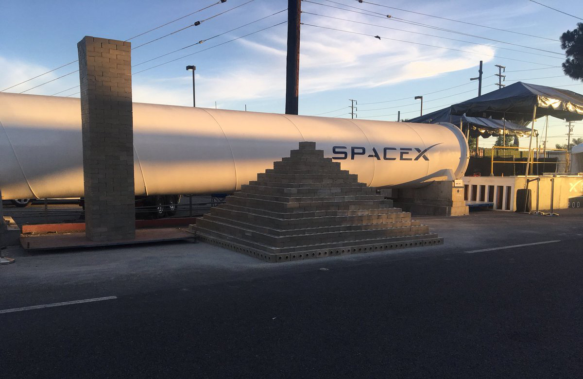 A pile of Boring Company-made bricks in front of a Hyperloop tube.