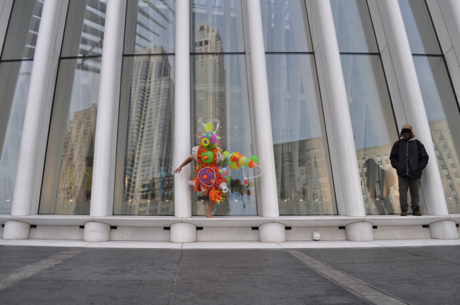 Photo of a person wearing a costume made of cheap plastic goods in front of the Oculus in New York City