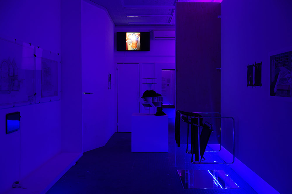 A view of a purple lit room with art installed. At the back is a screen.