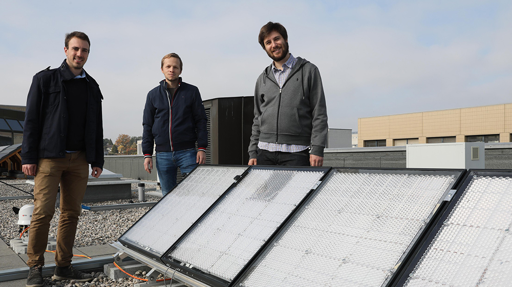 Photo of three people standing on a roof by solar panels
