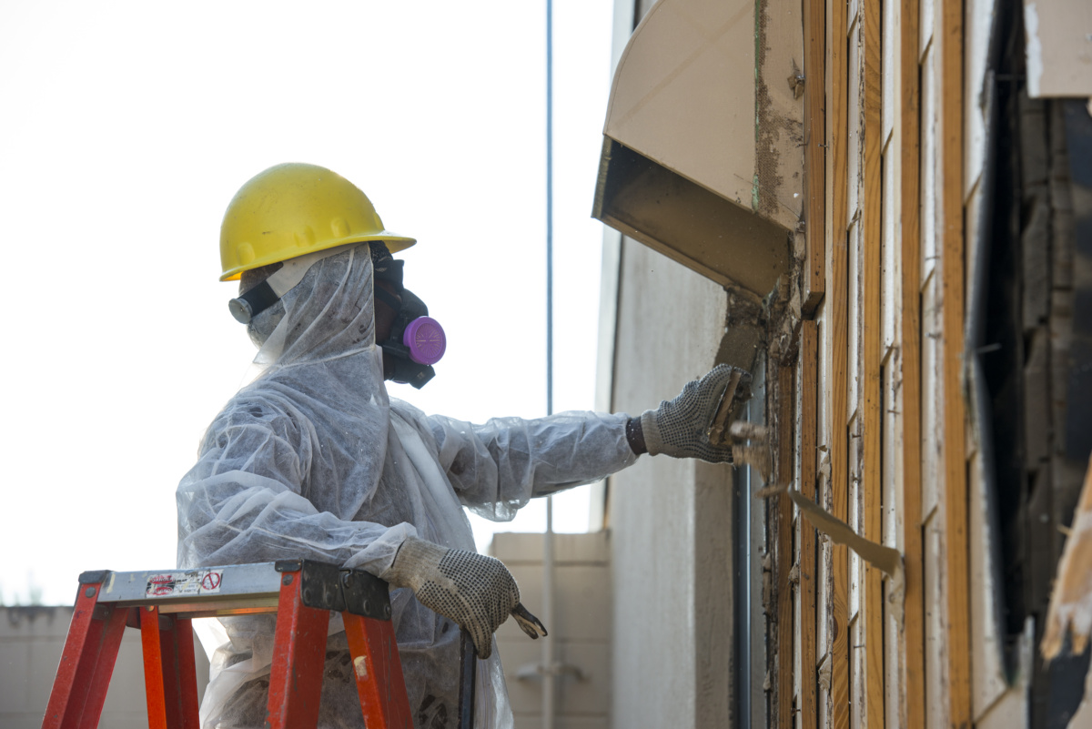 Photo of worker removing asbestos from building wall before demolition