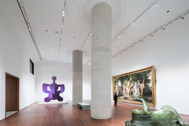 Photo of a white gallery with walnut floors and two concrete columns in the center