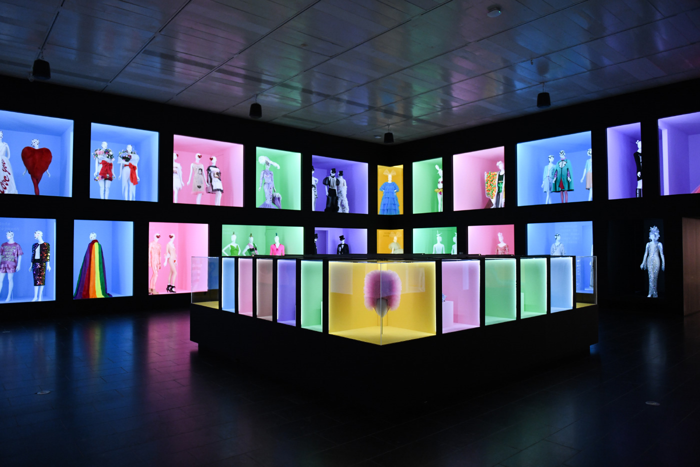 A blackened room with different colored boxes, each containing dresses, masks, and industrial design items