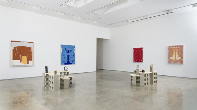 Installation photo of four paintings along with a series of small sculptures mounted on "plinths" made of cinderblocks.