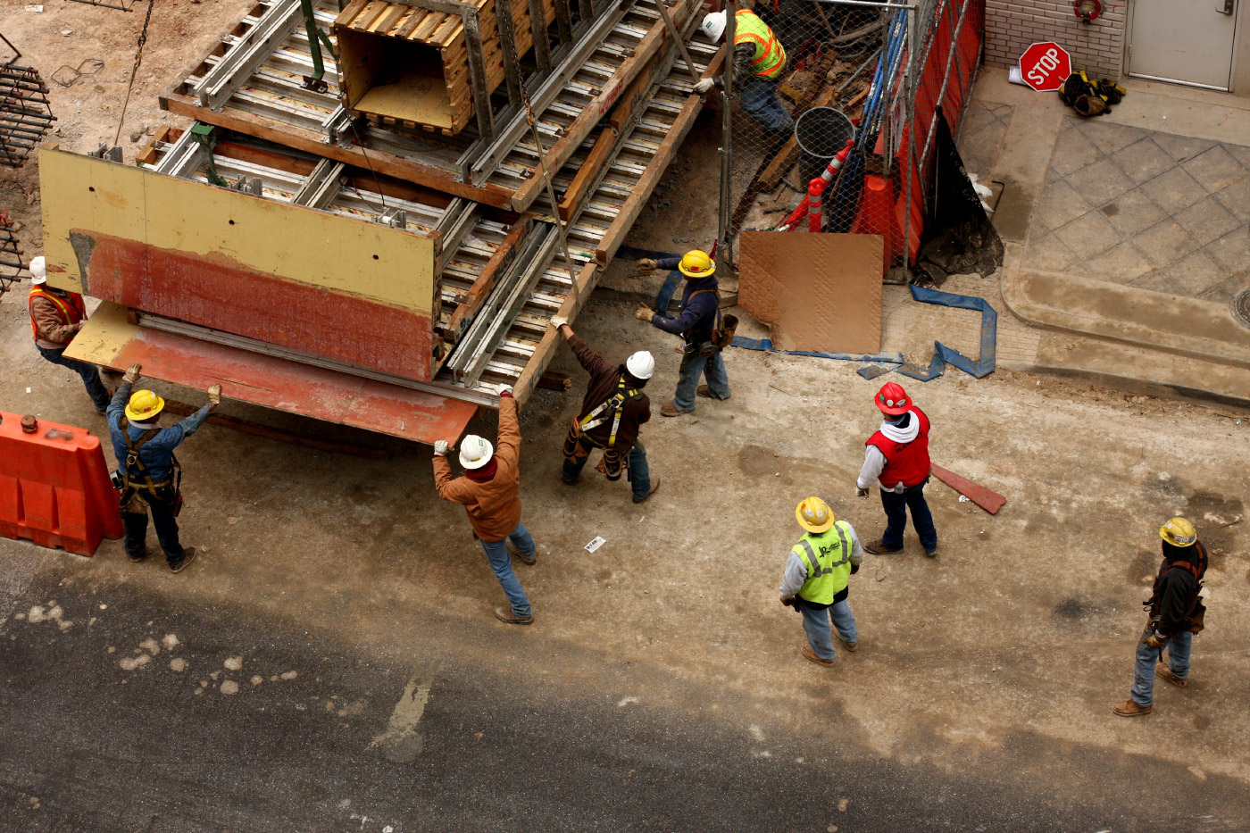 Photo of workers in hard hats and vests unloading construction materials from the back of a truck