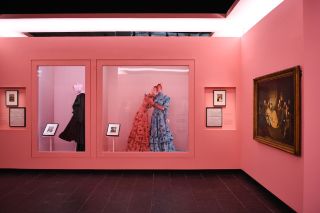 A pink wall and dresses behind a case