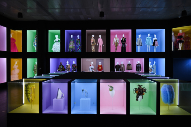A blackened room with different colored boxes, each containing dresses, masks, and industrial design items