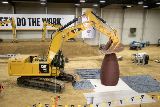 A backhoe pressing its arm down on a cylindrical concrete structure