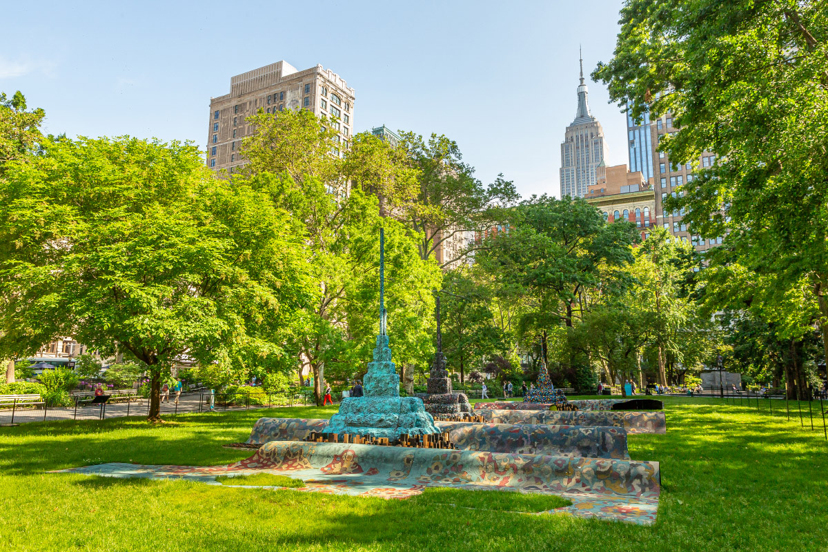 Photo of three stepped spires in Madison Square Park with the Empire State Building in the background