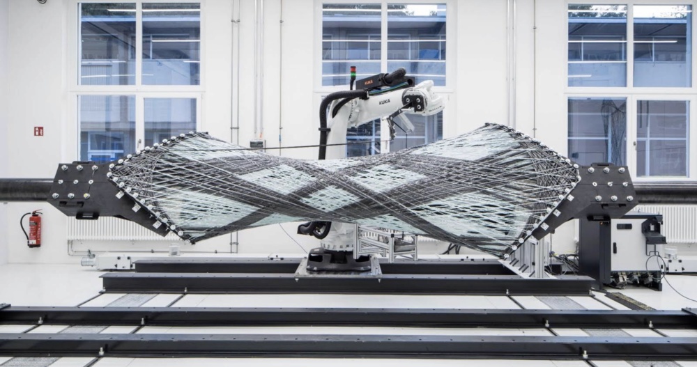 Photo of carbon fibers being woven by a robotic arm across two braces