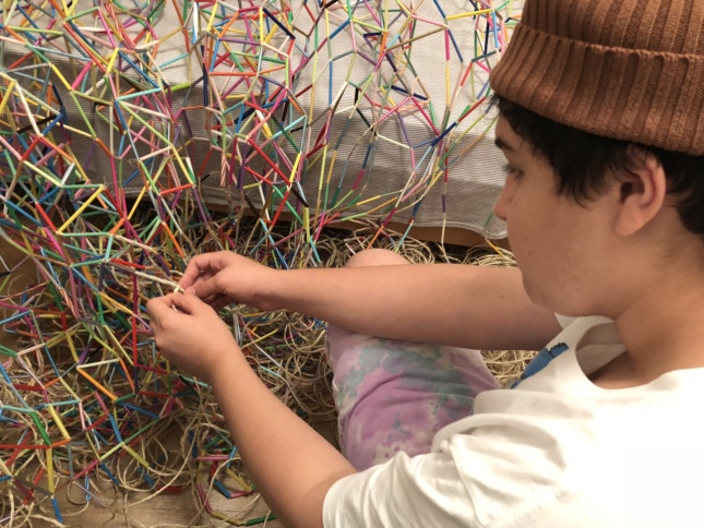 Photo of a teenager making a net out of colored plastic straws