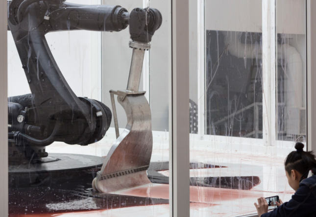 A robot arm with a squeegee end sweeping at a red liquid on the floor