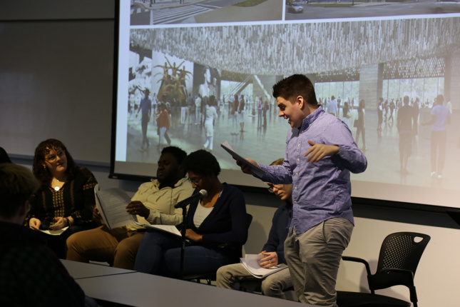 Photo of student standing up alongside panel of peers reading script 