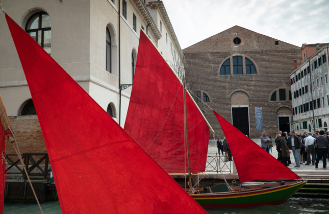 Red sailboats docked in front of a brick building