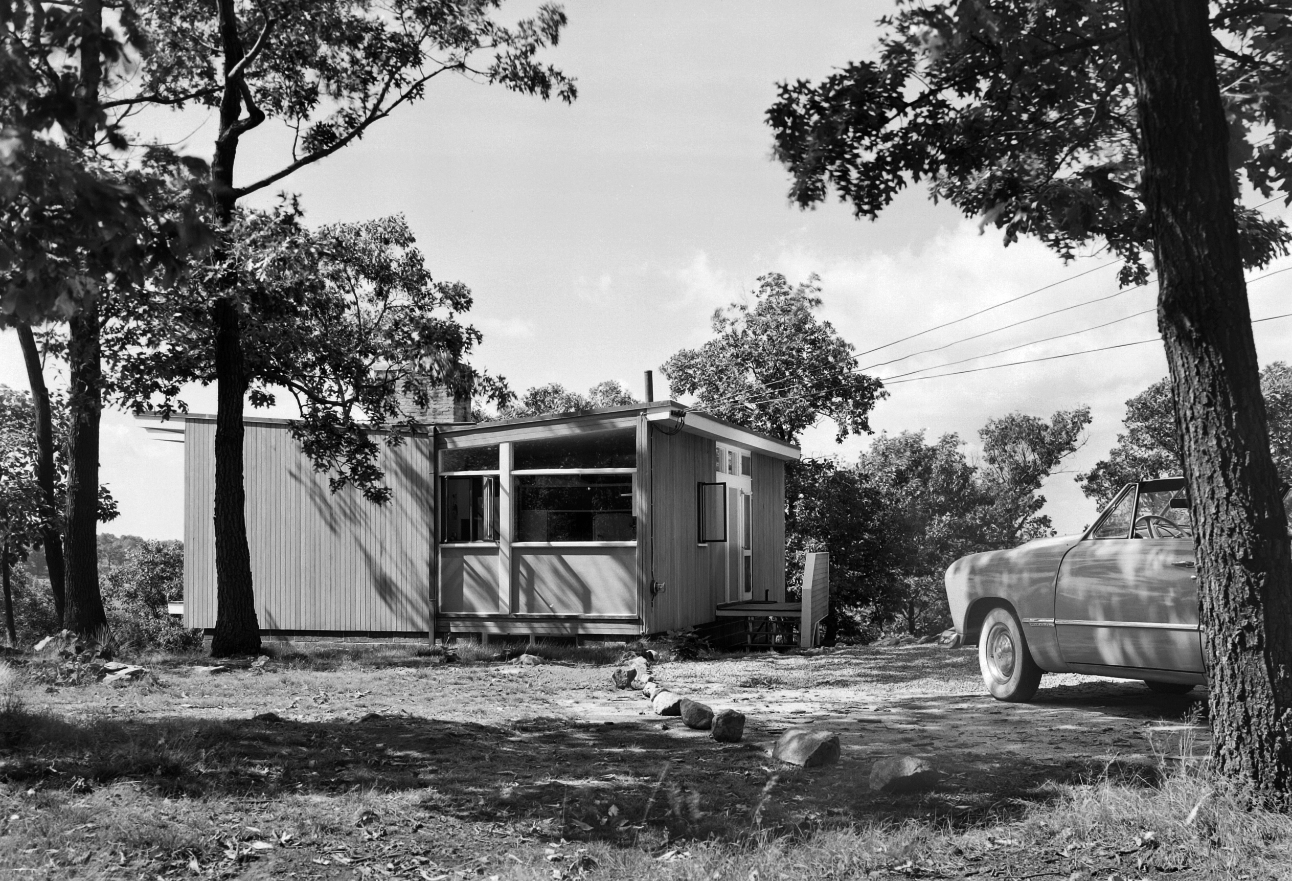 Black and white photo of a small house with a car in front