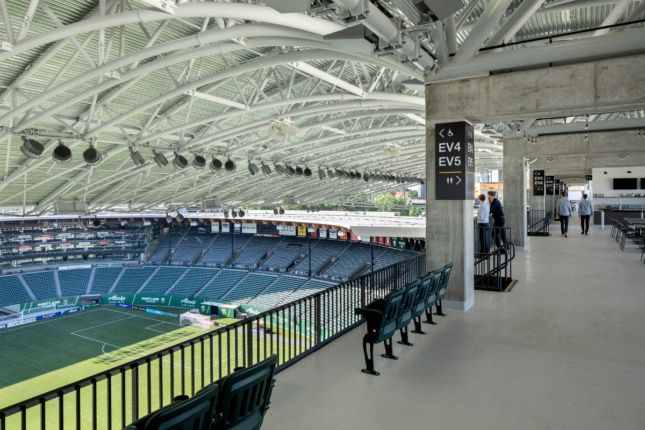 Photo of a stadium with a covered roof supported by white steel trusses