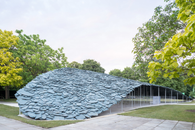 Photo of the 2019 Serpentine Pavilion, a low-slung building covered in slate tiles