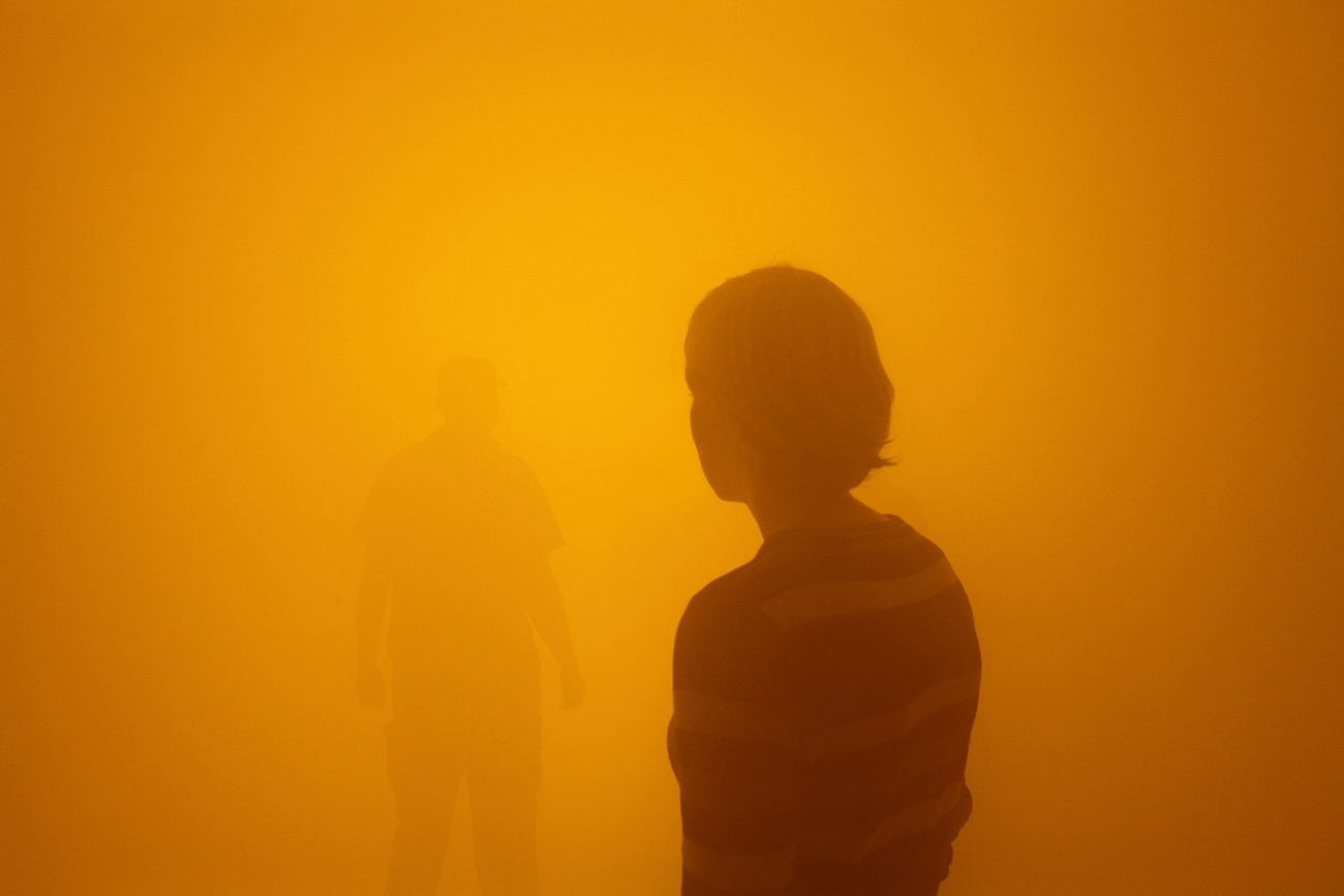 Two people wandering through an orange fog, at the Olafur Eliasson Tate show