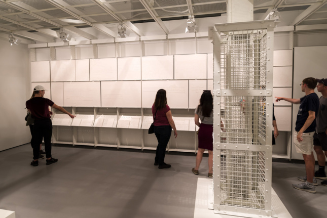 Installation view of several young people looking at wall of plaster, rectangular casts and a gas column