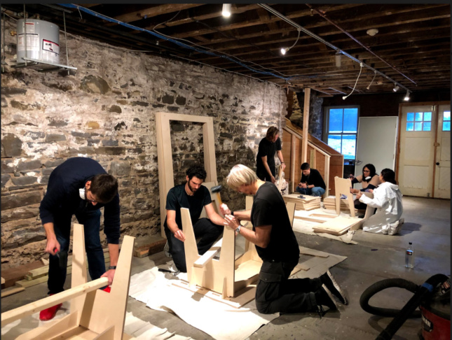 A group of students assembling furniture at the Kingston Creative Exchange, against a stone wall