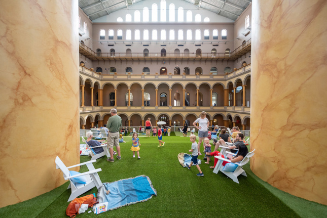 Image of white lawn chairs scattered with blue blankets and pillows between museum columns