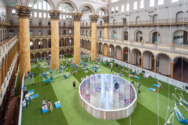 Aerial view of massive lobby of the National Building Museum with columns and green carpet laid out with people hanging out on blue hammocks and lawn chairs