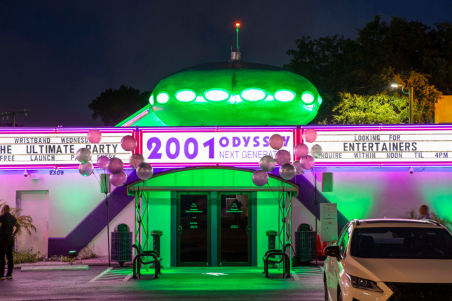 A strip club illuminated by green neon lights with a UFO-like Futuro house on top