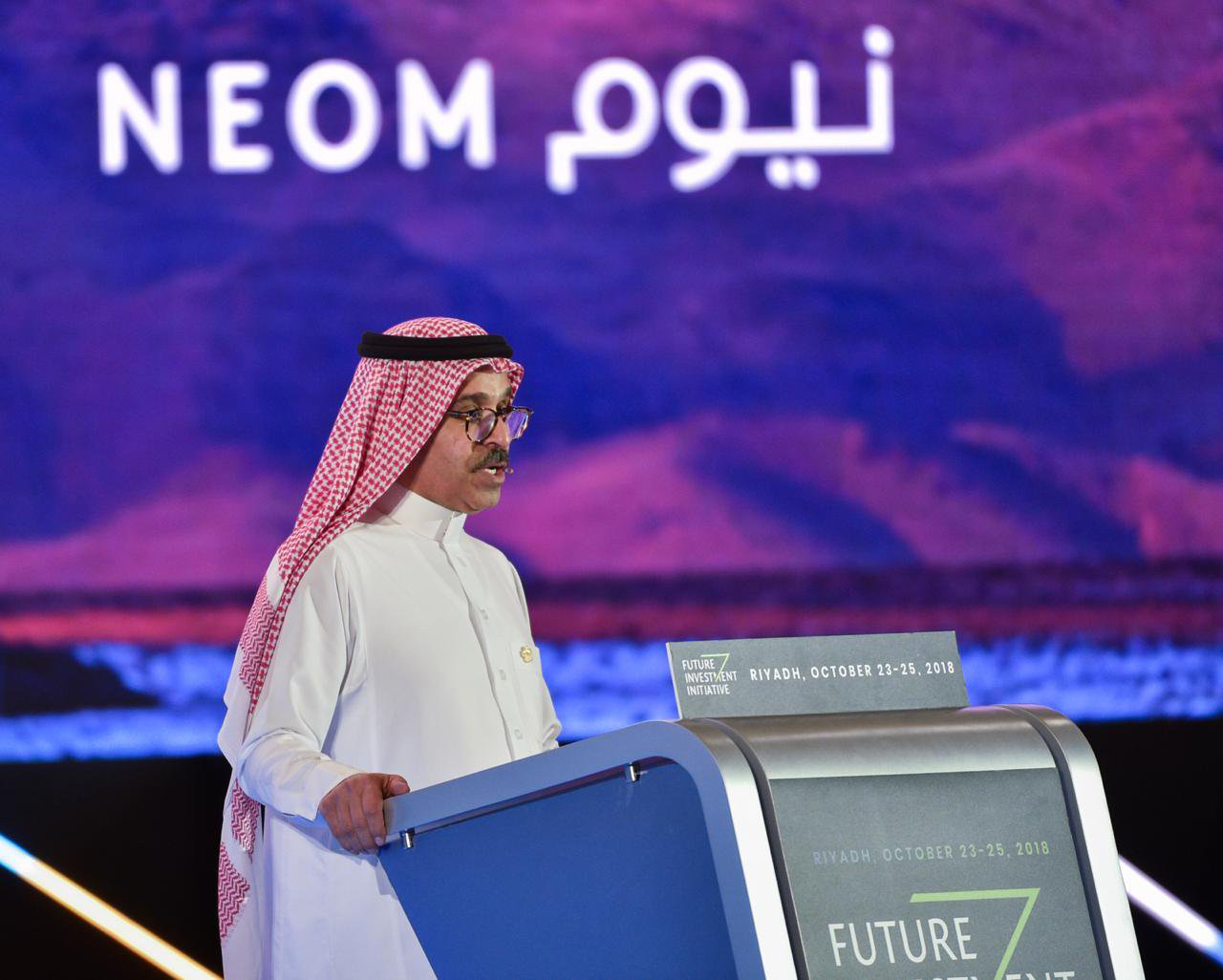 Image of man speaking at podium with purple sign behind him that says NEOM in English and Arabic