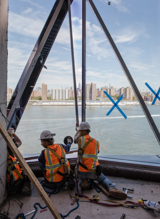 Installation image of workers installing glass panels at 10 Jay Street with Manhattan in the distance