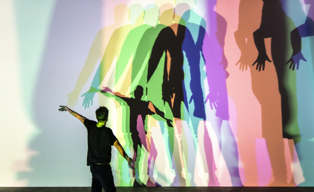 A person dancing in front of a screen with multi-colored duplicates in front of them