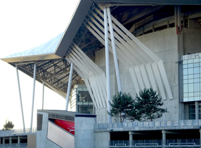 Side view of concrete arena with bracing that extends from wall to edge of canopy roof