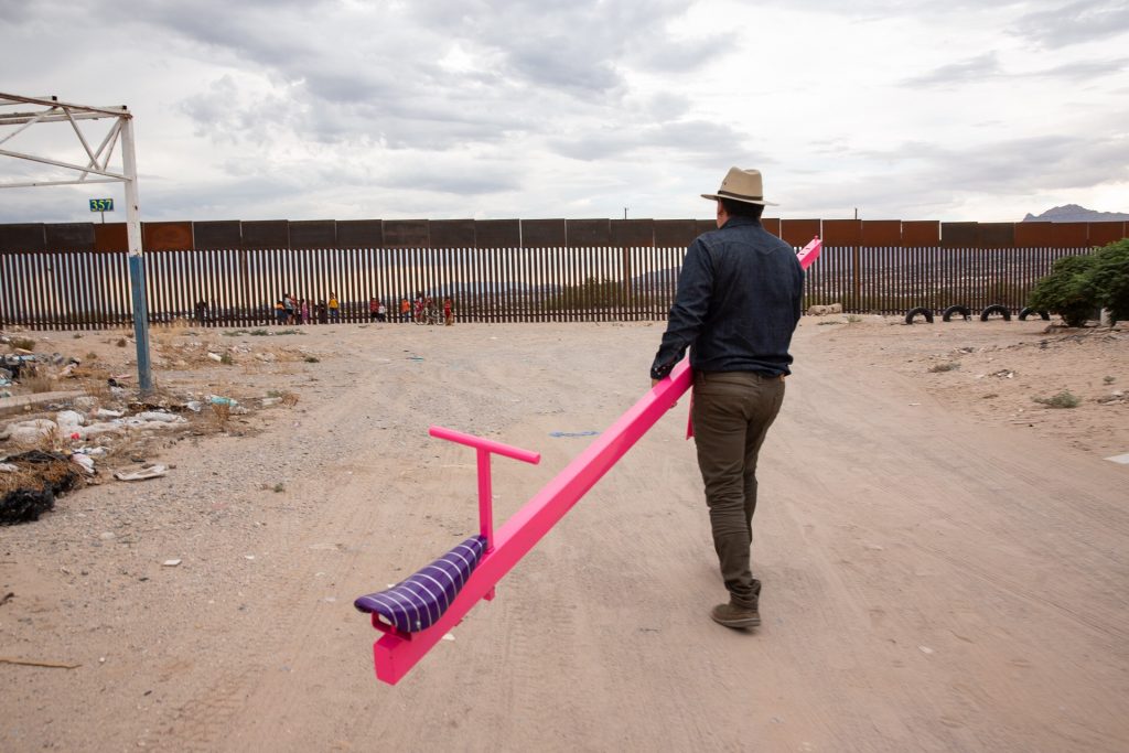 Man walking towards steel wall carrying a bright pink seesaw