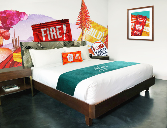 A taco bell themed hotel room with hot sauce shaped pillows and taco bell murals on the walls