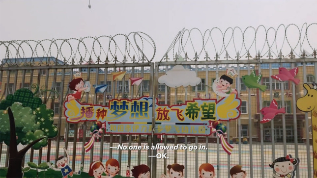 Screen still from VICE News film showing barbed wire fence in front of yellow school for children. Text on screen says "No one is allowed to go in."