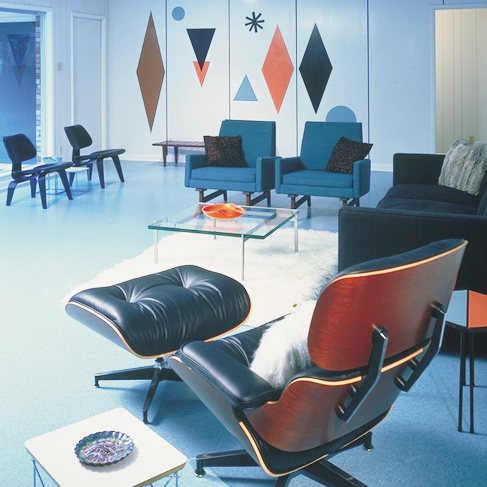 A lounge chair positioned infront of a living room, with a geometry wall mural composed of layers of laminate surfaves.