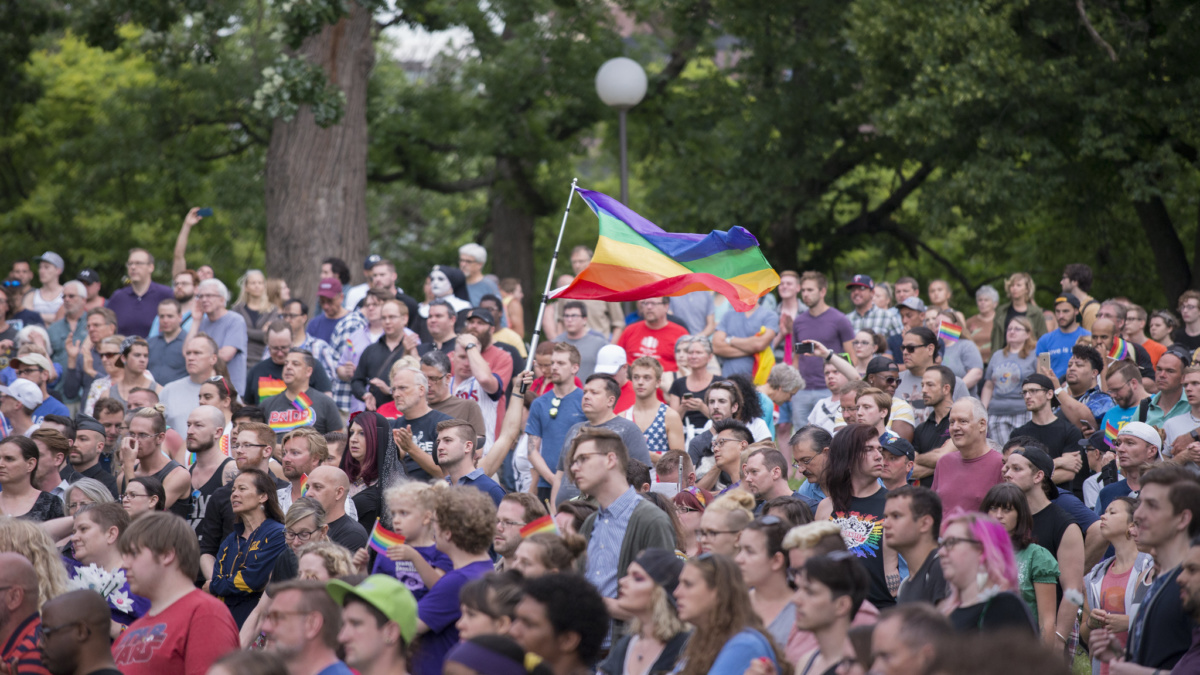 Image of people gathered at vigil, gay pride flag flown in air