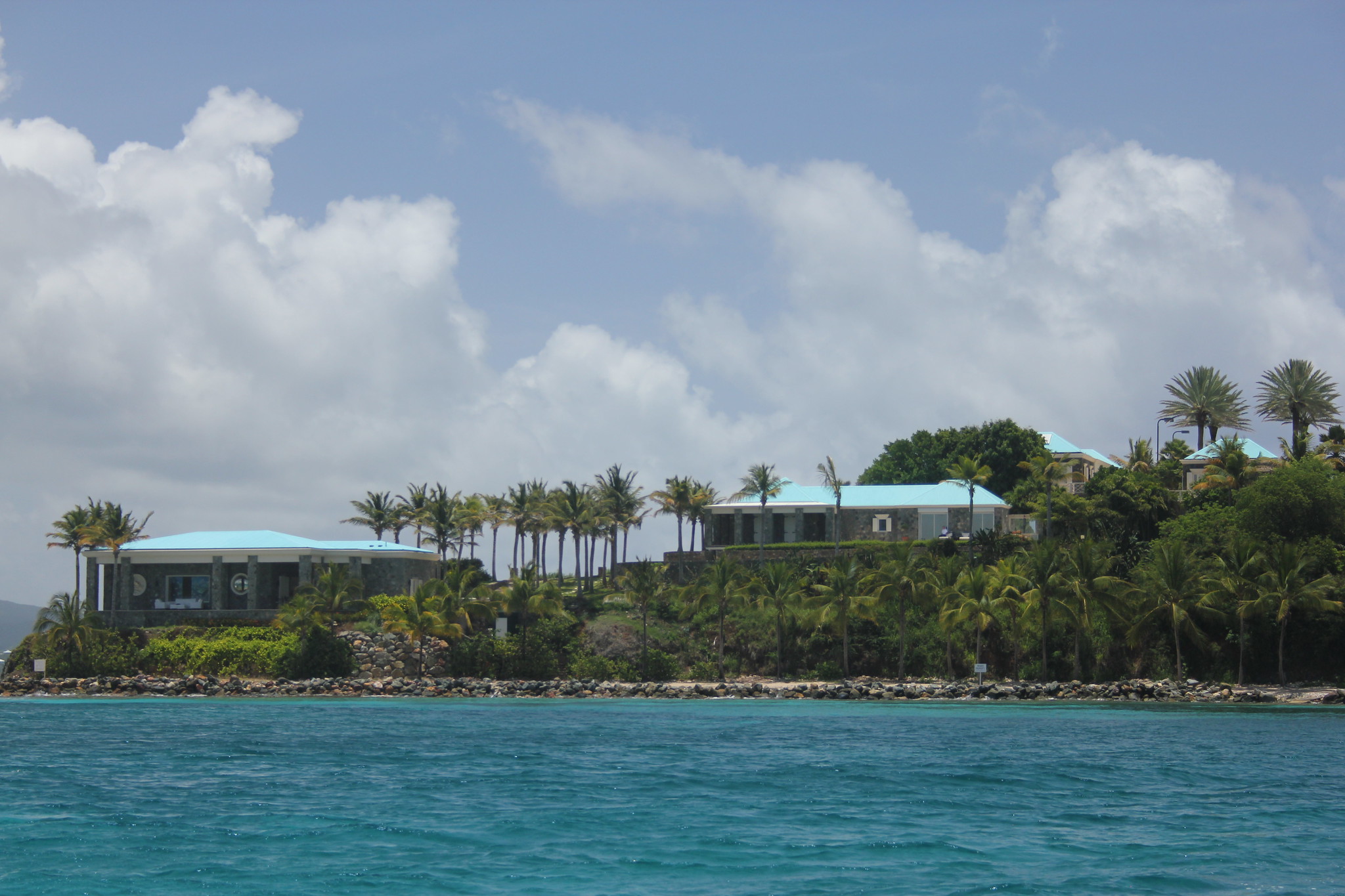 Two low slung buildings on a palm tree island above blue waters, where Jeffery Epstein vacationed