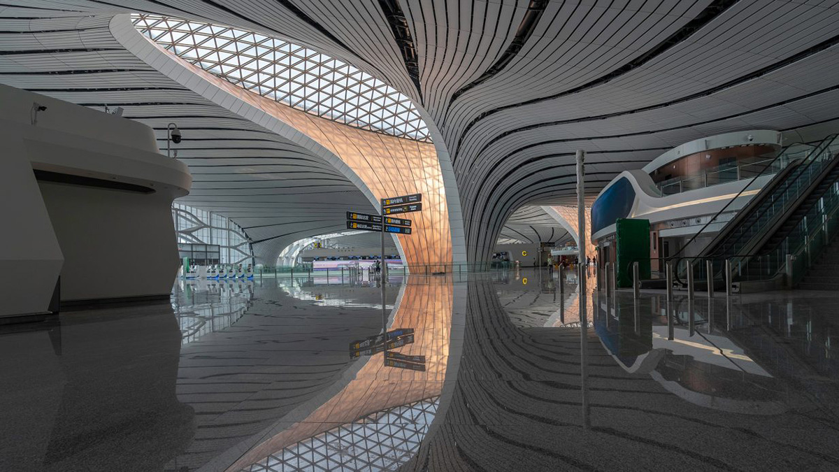 Interior photo of airport with sleek white floor and large skylight above curving walls next to check-in, the Beijing Daxing International Airport