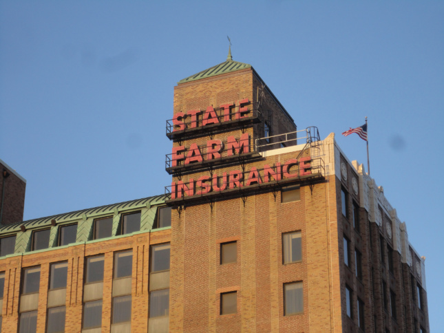 State Farm Insurange in bright red caps on top of a brown masonry building.