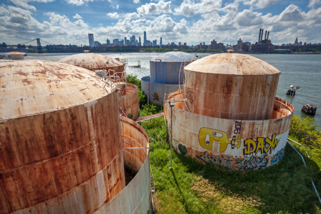 Rusty white oil tanks on a lawn next to a river in Bushwick Inlet Park