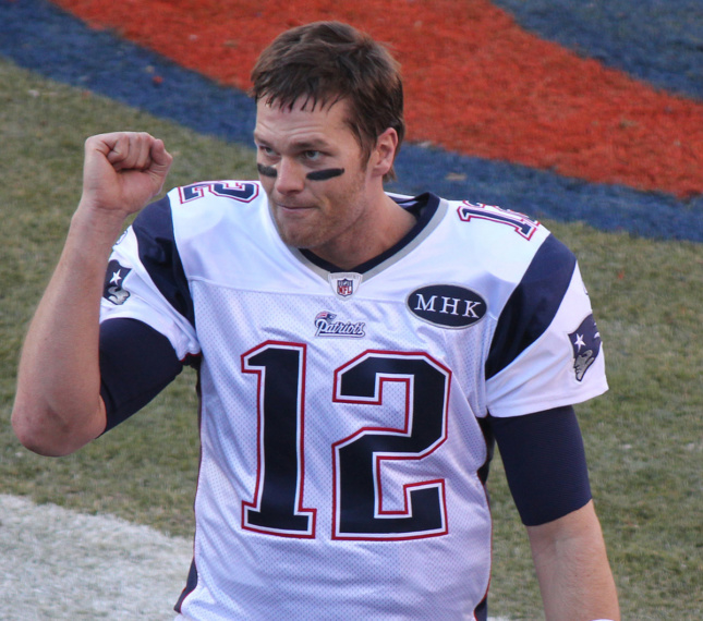 Image of a man in a football jersey, Tom Brady, on field with number 12 jersey and fist bump in air