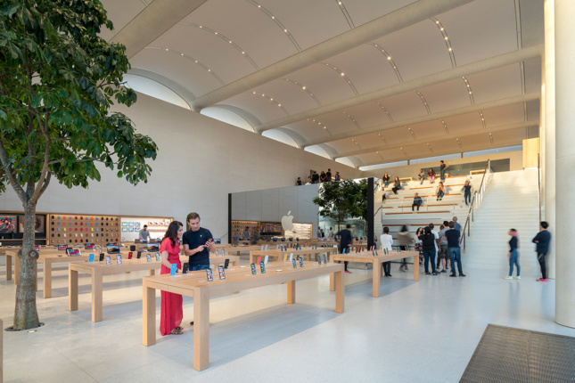 Interior shot of Apple store with tree, wooden display tables, terraced seating 