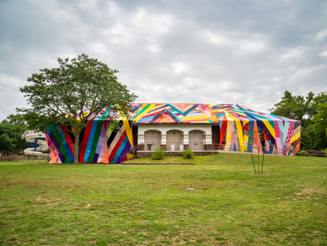 A large fabric patchwork "quilt" is draped over an entire building situated in a grassy expanse of a park in Grand Rapids.