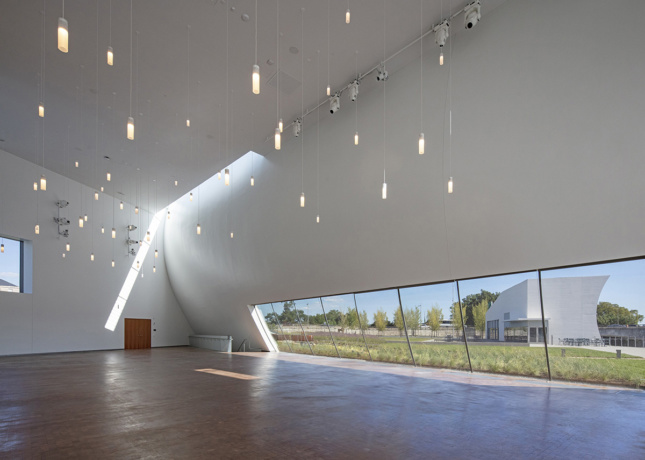 Interior image of white curved walls with light cutout in corner, fairy-like lights dangle from ceiling
