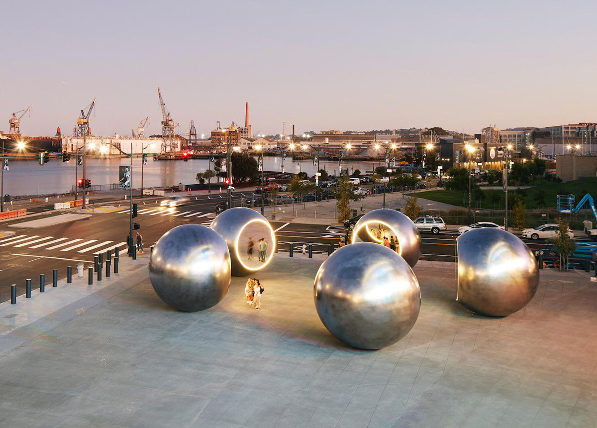 Bayside plaza with five shiny steel balls arranged in circle each lit up by ring of lights, designed by Olafur Eliasson