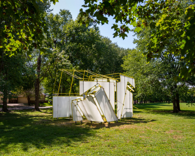 A white and yellow pipe pavilion below a grove of trees