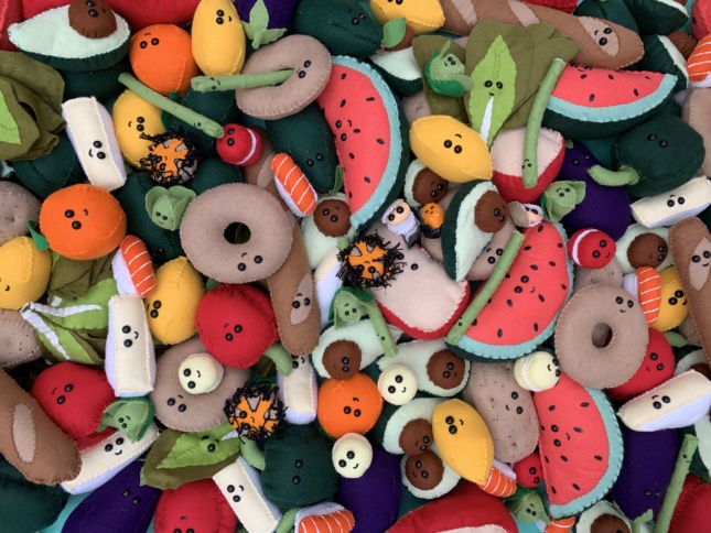 A pile of colorful foods with smiley faces and eye balls, completely made out of felt. 